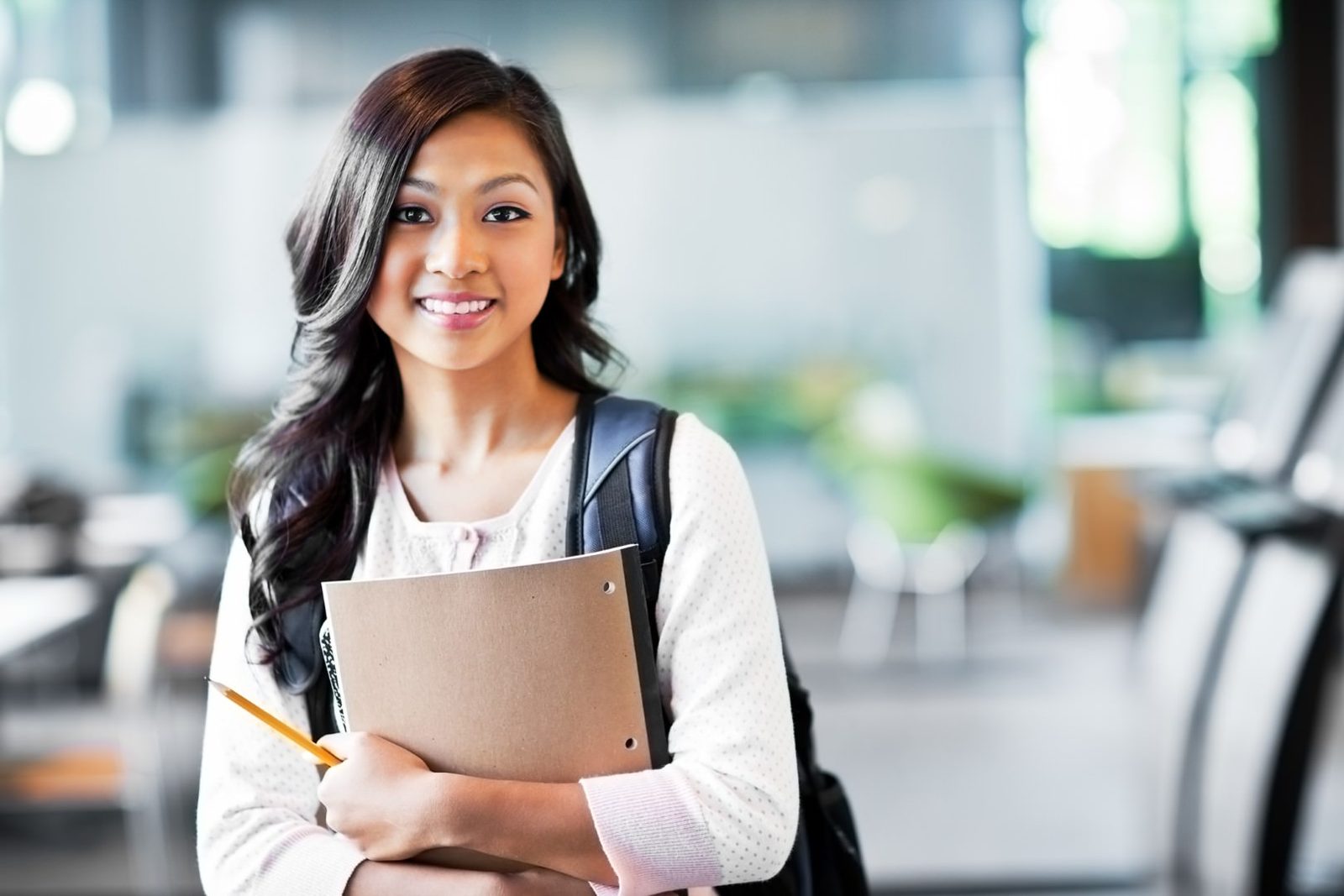 Smiling college student holding a notebook and backpack on campus